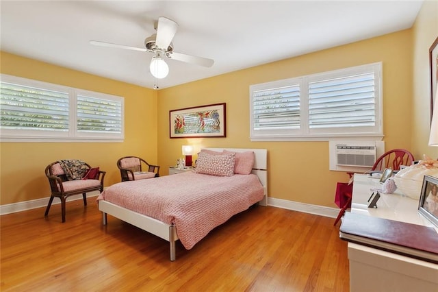 bedroom featuring light wood-style floors, baseboards, a ceiling fan, and a wall mounted AC