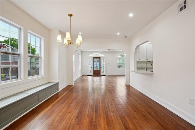unfurnished dining area with dark wood-type flooring, arched walkways, healthy amount of natural light, and recessed lighting