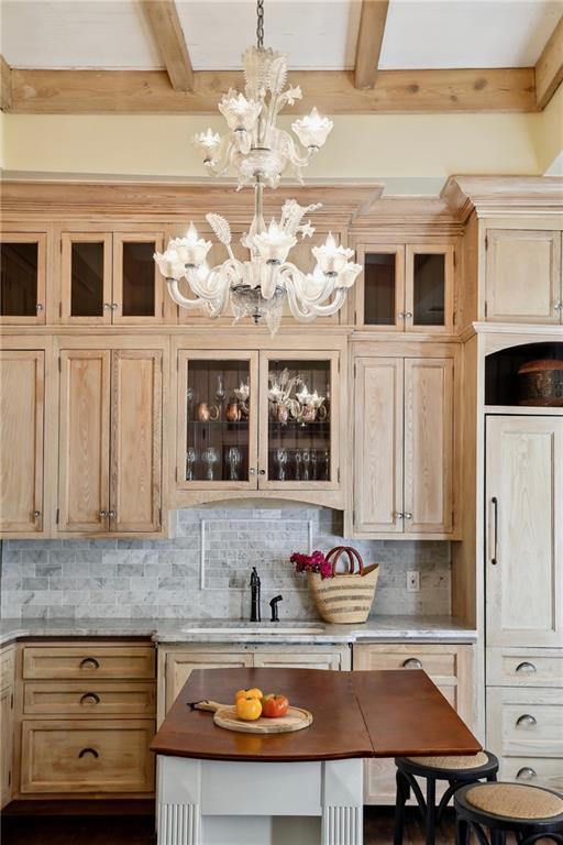 kitchen featuring a sink, decorative backsplash, beam ceiling, a chandelier, and glass insert cabinets