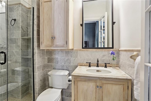 bathroom with tile walls, a stall shower, toilet, vanity, and wainscoting