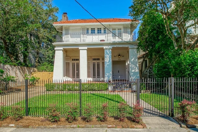 view of front of house featuring a balcony, a chimney, a fenced front yard, a porch, and a front lawn