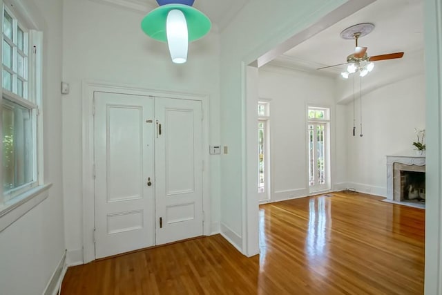 foyer entrance featuring a ceiling fan, baseboards, a high end fireplace, and wood finished floors