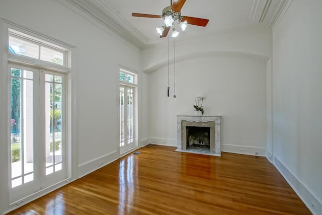 unfurnished living room with wood finished floors, a ceiling fan, a fireplace, crown molding, and baseboards