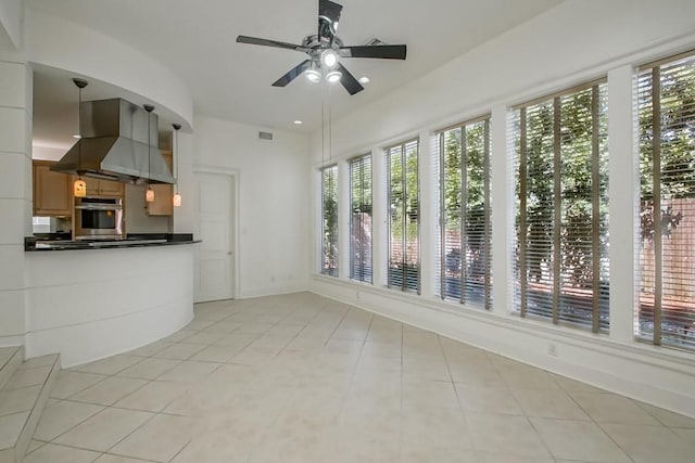 kitchen with a ceiling fan, light tile patterned floors, stainless steel oven, wall chimney range hood, and dark countertops