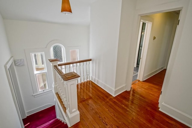 corridor with baseboards, an upstairs landing, and wood finished floors