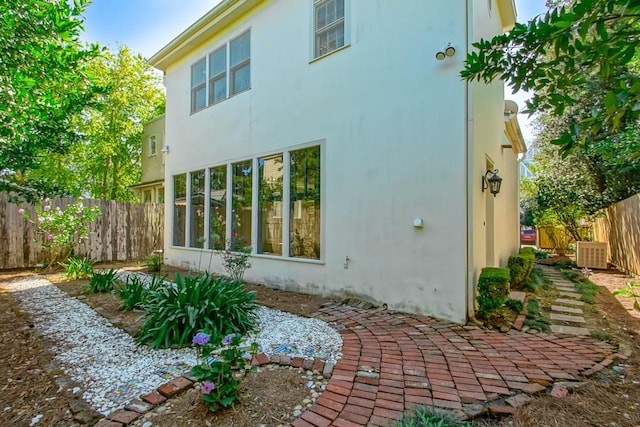 rear view of house with fence, stucco siding, and cooling unit