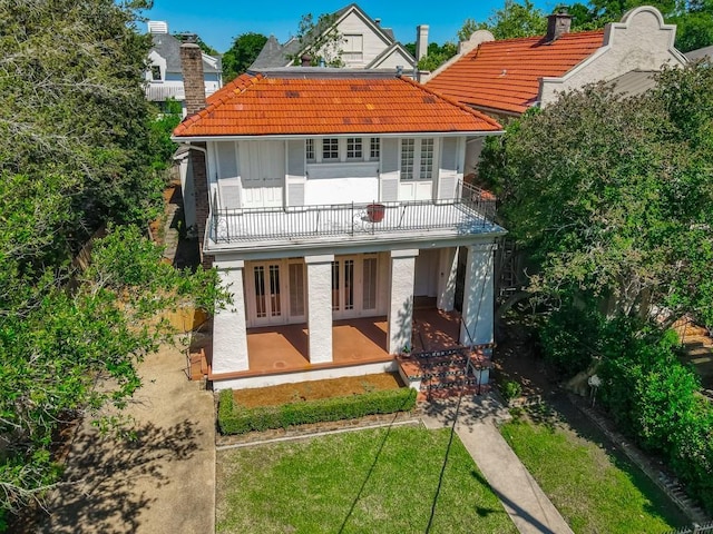 view of front of property with a balcony, french doors, a tiled roof, a patio area, and a front yard