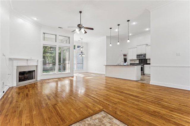 400 Brown Thrasher Loop, Madisonville, LA 70447 - unfurnished living room with a tile fireplace, ceiling fan with notable chandelier, crown molding, light wood-type flooring, and baseboards