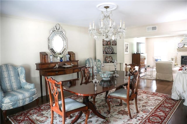 dining space with an inviting chandelier, visible vents, a brick fireplace, crown molding, and wood finished floors