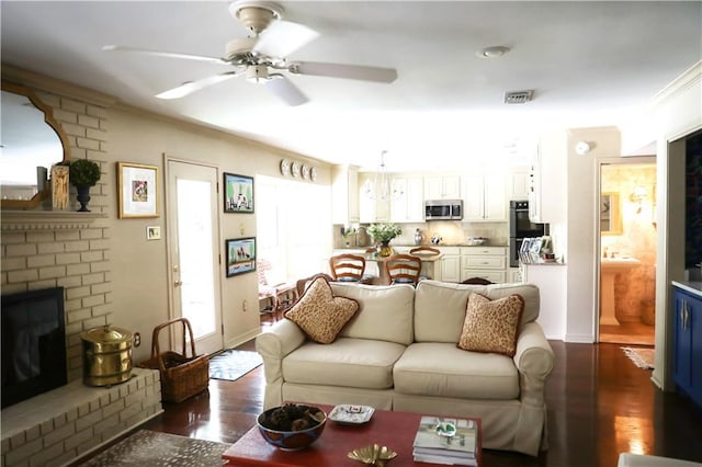living area featuring a ceiling fan, a fireplace, crown molding, and dark wood-type flooring