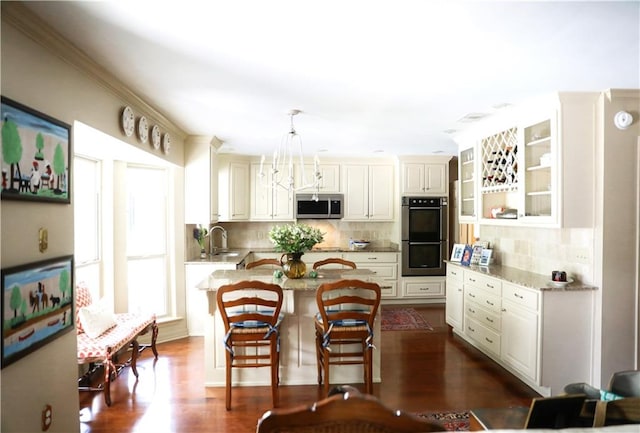 kitchen featuring a sink, light stone countertops, appliances with stainless steel finishes, a kitchen island, and tasteful backsplash