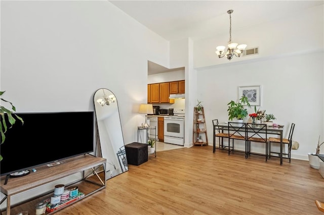 dining area featuring a chandelier, light wood-style floors, a towering ceiling, and baseboards