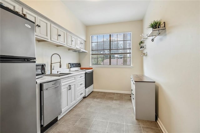 kitchen with appliances with stainless steel finishes, a sink, white cabinetry, baseboards, and light countertops