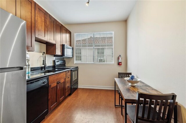 kitchen with black appliances, a sink, wood finished floors, dark countertops, and baseboards