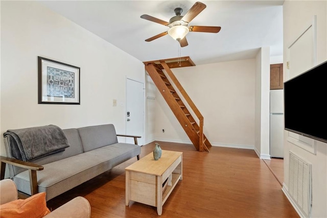 living area featuring a ceiling fan, stairway, light wood finished floors, and baseboards