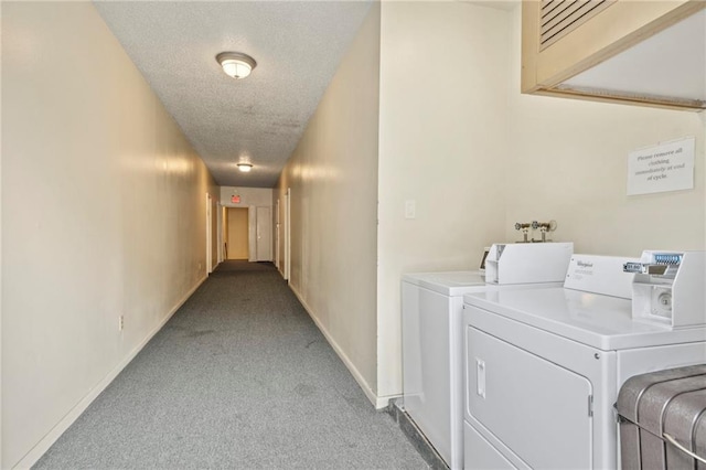 shared laundry with light colored carpet, washing machine and dryer, a textured ceiling, and baseboards