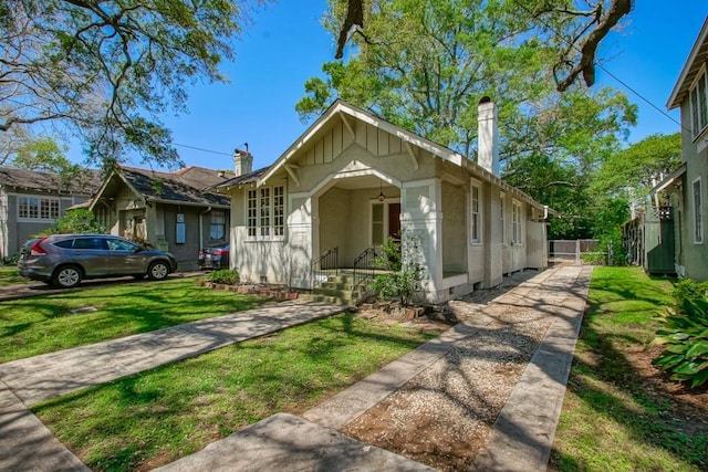 bungalow-style house featuring fence, stucco siding, a chimney, and a front yard