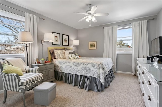 bedroom featuring light colored carpet, multiple windows, baseboards, and a ceiling fan