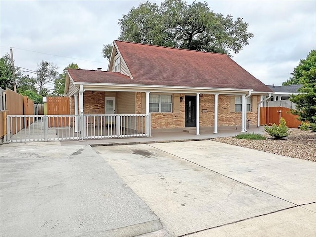 view of front facade featuring covered porch, a gate, fence, brick siding, and a shingled roof
