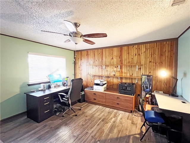 office area with wood finished floors, a ceiling fan, a textured ceiling, visible vents, and wooden walls