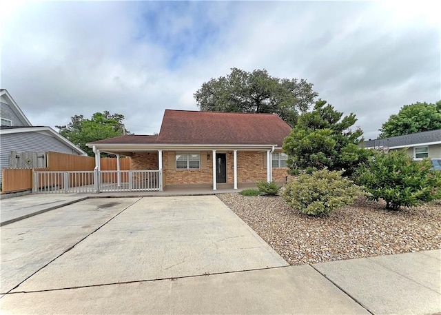 view of front of home featuring covered porch, brick siding, driveway, and fence