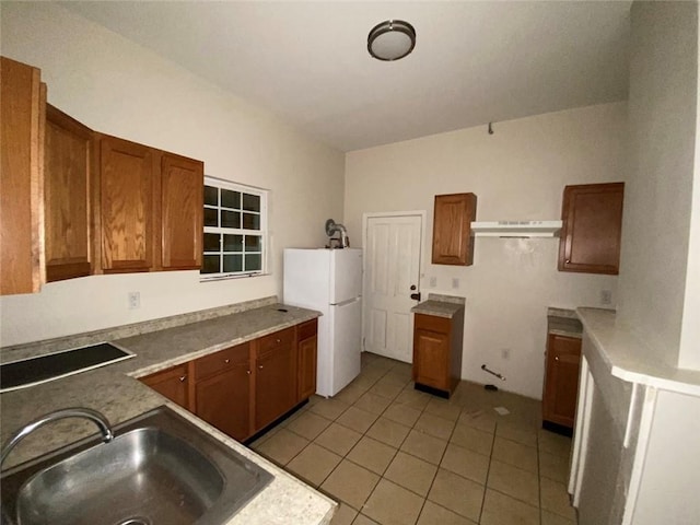 122628 Carondelet St, New Orleans, LA 70130 - kitchen featuring freestanding refrigerator, under cabinet range hood, light tile patterned floors, a sink, and brown cabinets