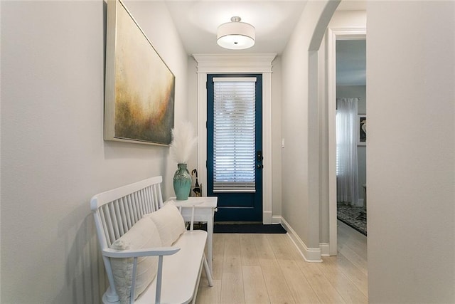 doorway to outside with baseboards, light wood-style floors, and arched walkways