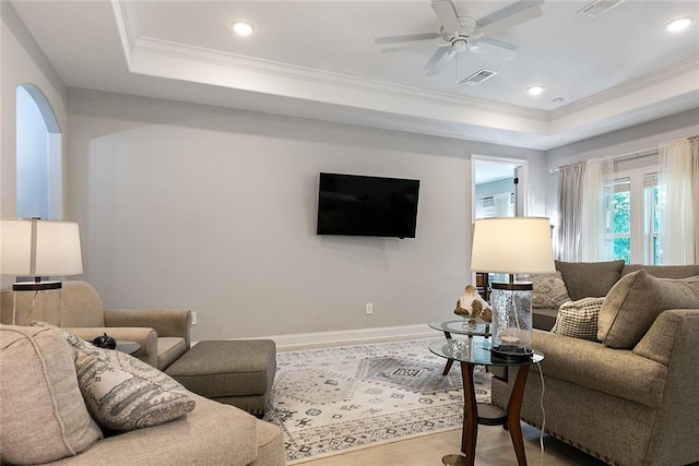 living room featuring a ceiling fan, baseboards, ornamental molding, wood finished floors, and a raised ceiling
