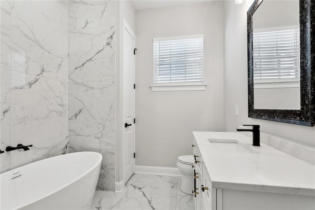 bathroom with baseboards, marble finish floor, toilet, vanity, and a soaking tub