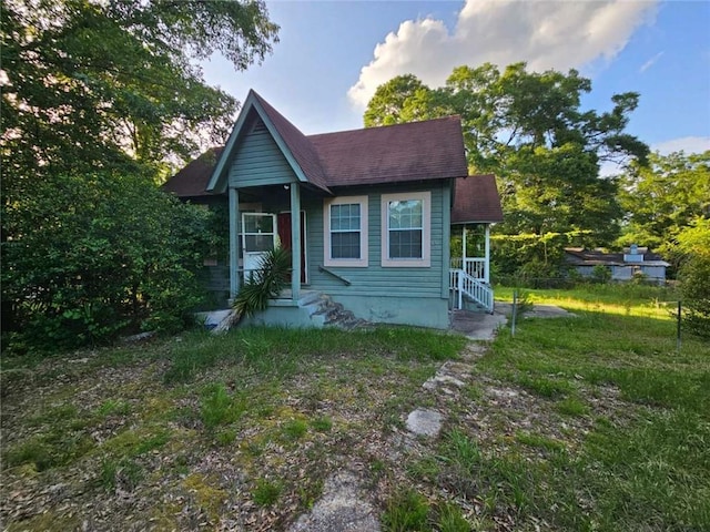 bungalow-style home with roof with shingles, entry steps, and a front lawn
