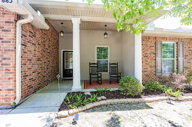 view of exterior entry featuring covered porch, stucco siding, and brick siding