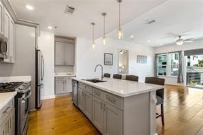 kitchen featuring gray cabinets, stainless steel appliances, a sink, a kitchen breakfast bar, and wood finished floors