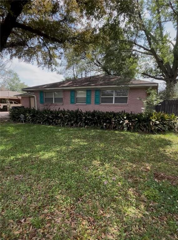 view of front facade featuring brick siding, a front lawn, fence, and a carport