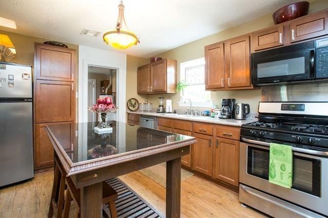 kitchen featuring appliances with stainless steel finishes, brown cabinetry, light wood-style flooring, and a sink