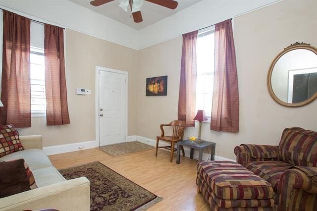 living area with a ceiling fan, baseboards, a healthy amount of sunlight, and wood finished floors