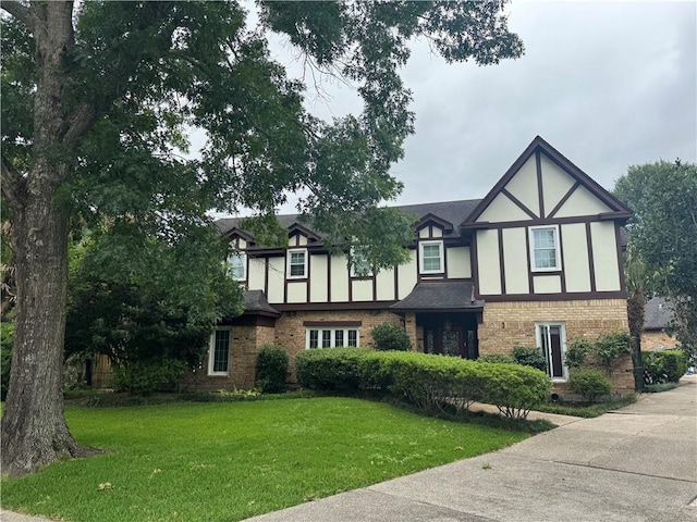 english style home with roof with shingles, stucco siding, a front lawn, and brick siding