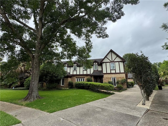 tudor house featuring stucco siding, brick siding, and a front lawn
