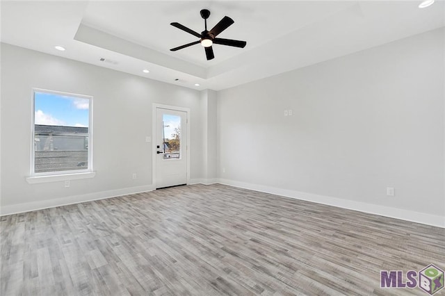 unfurnished room with a tray ceiling, baseboards, and wood finished floors