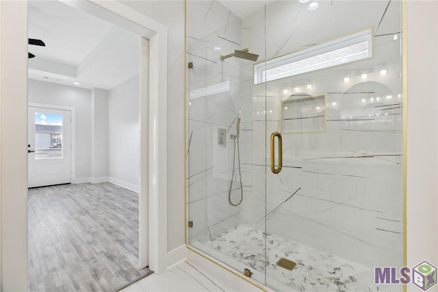 full bath featuring wood finished floors, a marble finish shower, and baseboards