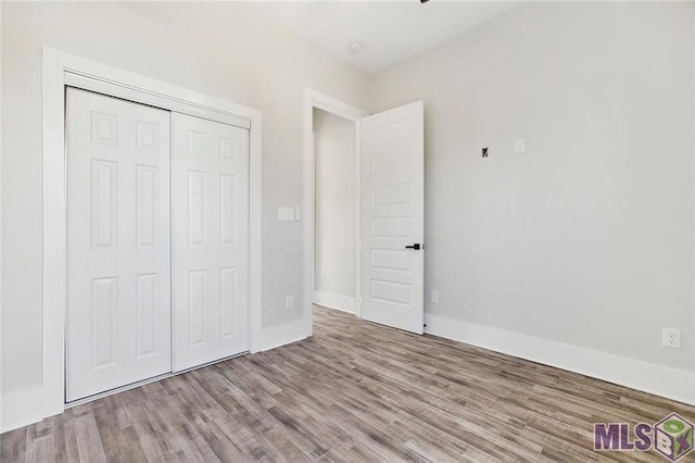 unfurnished bedroom with a closet, wood finished floors, and baseboards