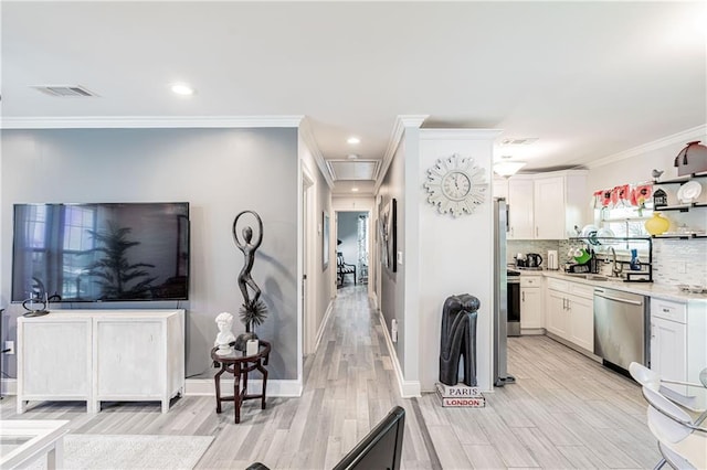 kitchen featuring stainless steel appliances, light wood finished floors, a sink, white cabinets, and crown molding
