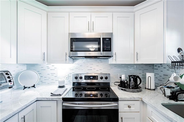 kitchen featuring appliances with stainless steel finishes, white cabinets, decorative backsplash, and light stone counters