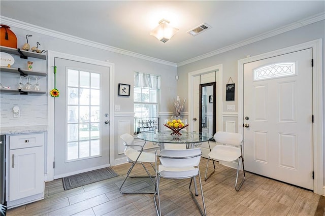 dining room featuring light wood-style flooring, a wainscoted wall, ornamental molding, and a decorative wall