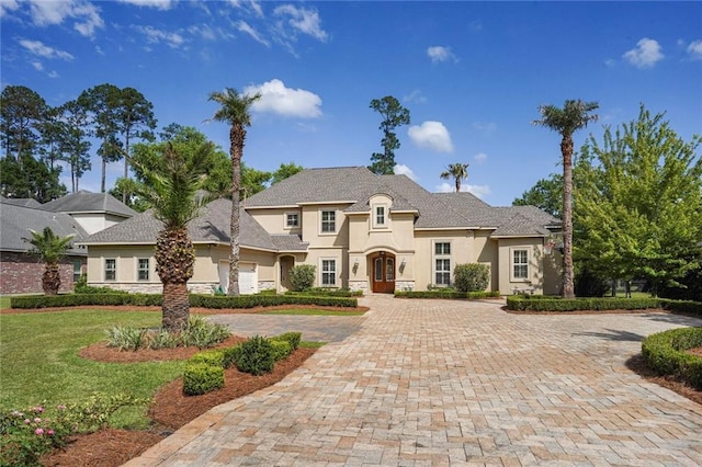 french country style house with stucco siding, a front yard, and stone siding