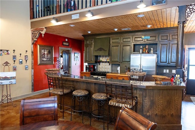 kitchen featuring stainless steel appliances, wood ceiling, baseboards, a kitchen bar, and a peninsula