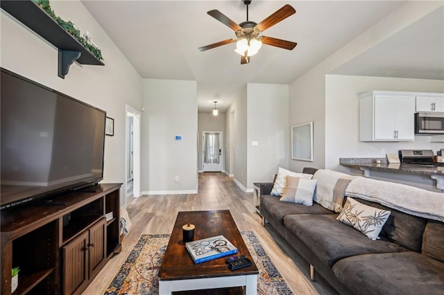 living area with light wood-style floors, a ceiling fan, and baseboards