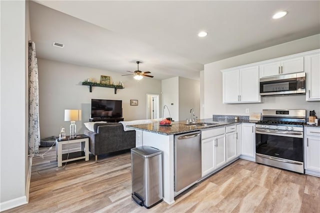 kitchen with stainless steel appliances, a sink, white cabinetry, a peninsula, and light wood finished floors