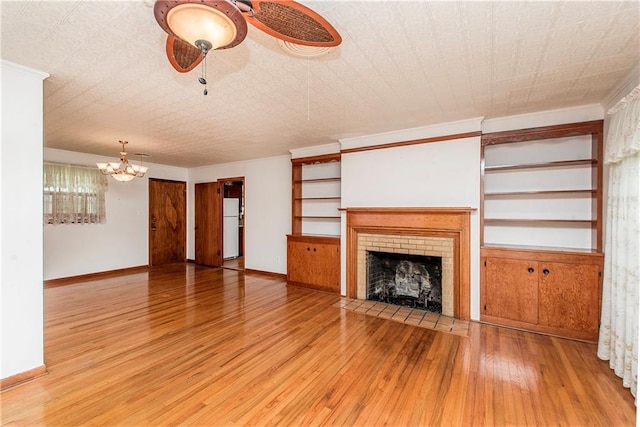 unfurnished living room with light wood-style flooring, a chandelier, ceiling fan, a fireplace, and baseboards