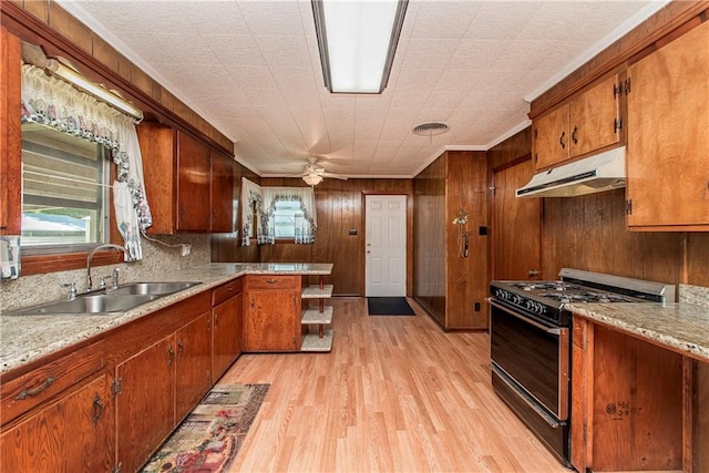 kitchen featuring black gas range, under cabinet range hood, a sink, light wood-type flooring, and brown cabinetry