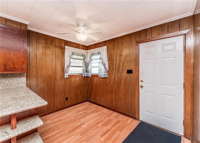 entryway with a ceiling fan, light wood-type flooring, wooden walls, and crown molding